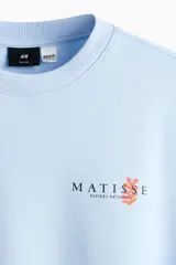 Buzo celeste de corte holgado con hombros caídos y cuello redondo. Presenta un pequeño estampado en el pecho con la inscripción "Matisse" y un detalle gráfico en color naranja.