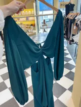 Vestido largo color bordó con escote en V profundo, detalle de nudo central y aberturas laterales en la cintura. Presenta mangas largas abullonadas con puños elásticos y falda con tajo frontal pronunciado.