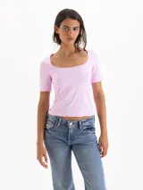 Top de silueta ajustada y largo hasta la cadera, confeccionado en tejido de punto liso color rosado. Presenta un escote ovalado profundo y mangas cortas de calce ceñido.