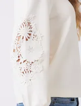 Buzo blanco de modal, corte clásico, con mangas largas abullonadas y apliques de crochet floral en los hombros y parte superior de las mangas.