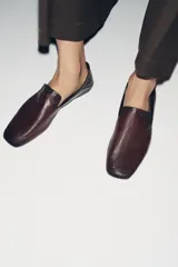 Zapato plano tipo slipper confeccionado en piel color bordó, con diseño de copete subido, punta cuadrada y talón flexible que permite su uso como destalonado.