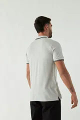 Remera polo negra de manga corta con ajuste regular. Presenta cuello y puños con ribete a rayas en gris y bordó. El logo de la marca está estampado en el pecho.