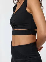 Crop top deportivo negro con fruncido frontal en el pecho, tirantes anchos y aberturas inferiores que dejan al descubierto la zona bajo el busto, confeccionado con tecnología Aloe Vera.