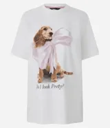 Remera blanca de algodón con cuello redondo y mangas cortas. Presenta una gran estampa central de un perro de raza cocker spaniel con un gran lazo rosa atado al cuello, y el texto "Do I look Pretty?" debajo.