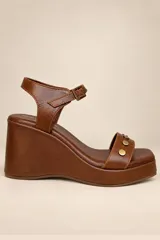 Sandalias de plataforma con cuña, confeccionadas en cuero negro con punta cuadrada y plantilla metalizada. Tienen una tira delantera decorada con tachas metálicas redondas y una tira al tobillo con hebilla regulable.