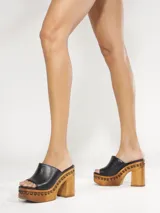 Zueco de plataforma Schutz color negro con taco alto de madera y detalles de tachas alrededor de la suela.