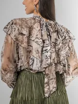Camisa de seda italiana con diseño reversible, permitiendo usar el lazo en la parte frontal o posterior. Presenta un estampado sutil con motivos abstractos y animal print, cuello alto con volados, mangas largas con puños elásticos y corte holgado.