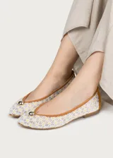 Bailarina de diseño artesanal confeccionada en rejilla bordada con motivo de flores pequeñas, con refuerzo en el talón de ante color camel y ribete a juego. Presenta un detalle de media esfera metálica dorada en la puntera y suela plana de cuero.