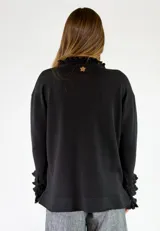 Saco de punto negro con cierre frontal, manga larga con volados en los puños y detalles de volados en el cuello y el ruedo.