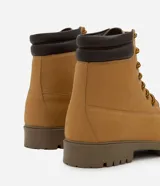 Bota estilo worker de caña media con acabado tipo nobuck. Presenta puntera redondeada, cuello acolchado en contraste, cierre con cordones y ojalillos metálicos. Cuenta con suela dentada de goma para mayor tracción.
