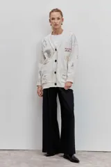 Cardigan de punto azul con cuello en V, cierre frontal de botones y bolsillos delanteros. Presenta bordados decorativos con motivos variados y frases en colores contrastantes.