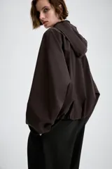 Cazadora de cuello subido con capucha ajustable, manga larga con puños elásticos y bolsillos delanteros con solapa. Presenta bajo elástico y cierre frontal con cremallera oculta y botones a presión.