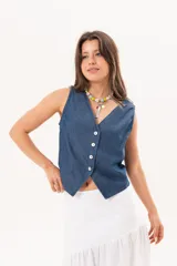 Chaleco de denim fino y liviano azul, de silueta entallada con escote en V, cierre frontal de botones de nácar y diseño con terminación en puntas en la delantera.
