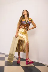 Falda midi de tiro alto y silueta ajustada, color dorado, confeccionada en cuero con tajo lateral y flecos largos en la parte inferior del frente.