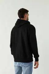 Buzo de felpa negro con capucha, cordones ajustables y bolsillo tipo canguro. Tiene puños y cintura acanalados, y logo en grifa de plástico.