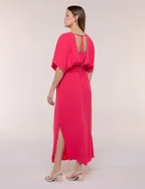 Vestido largo amarillo de corte fluido con escote en V, mangas cortas amplias y apliques de tachas en el escote y puños. Posee cintura elastizada fruncida y falda larga con tajos laterales en el ruedo.