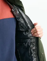 Campera acolchada de color gris, con capucha desmontable, cierre frontal y bolsillos laterales con cremallera. Presenta un diseño de costuras horizontales y detalles en color naranja en los tiradores de los cierres.