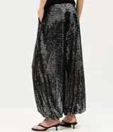 Pantalón balloon negro de poliéster con aplicación integral de lentejuelas brillantes, de corte amplio en las piernas y puños ajustados en los tobillos con cintura elástica.