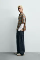 Camisa de corte boxy fit confeccionada en tejido de algodón, con estampado de cuadros en tonos tierra. Presenta cuello solapa, manga corta y cierre frontal de botones.