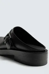 Zueco destalonado negro con hebilla en el empeine y suela a tono con tacón bajo.