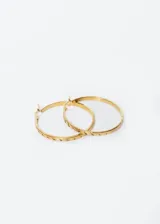 Aros tipo argolla de acero quirúrgico color dorado con cierre a presión y diseño de surcos grabados.
