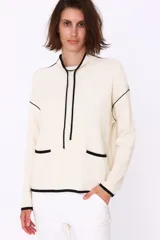 Sweater color crema con cuello alto, corte holgado y detalles en negro en cuello, puños, ruedo y bolsillos frontales.