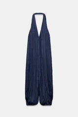 Mono largo satinado de color azul marino, con cuello halter, escote en V profundo y espalda descubierta. Presenta diseño plisado y bajo abullonado con terminación en puño.