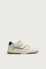 Zapatilla deportiva de estilo retro con diseño de paneles en combinación de materiales. Presenta una base de color blanco con detalles en verde oscuro y gris, y una suela de goma con volumen en tono caramelo.
