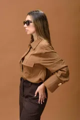 Camisa color habano de corte clásico, con cuello camisero, bolsillos frontales con solapa y puños anchos con detalle de botón metálico.