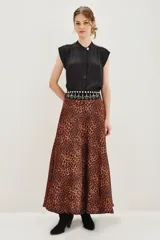 Falda larga de corte acampanado con estampado animal print de leopardo en tonos caramelo y negro. Presenta una cintura alta con detalle de banda decorativa con tachas metálicas.