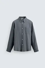 Camisa de corte relajado confeccionada en tejido fluido con mezcla de viscosa, presenta un diseño de rayas verticales, cuello solapa, cierre frontal con botones, manga larga con puño abotonado y un bolsillo de plastrón en el pecho.