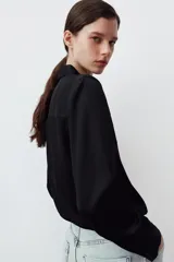 Camisa de satén con cuello solapa, manga larga con puños y bajo ajustable mediante cordones. Presenta cierre frontal con botones ocultos.