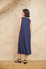 Vestido midi azul con textura crepé, escote en V, sin mangas, bolsillos laterales y aplique de flor con piedras facetadas en el escote.