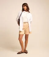 Short de sastrería color beige, de corte recto con pinzas delanteras y trabillas en la cintura. Incluye un cinturón de poliuretano a tono con hebilla metálica dorada.