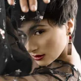 Par de aros colgantes con forma de labial dorado con glitter, tapa roja y estrella dorada en la parte superior.