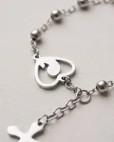 Pulsera tipo rosario de acero con baño de plata, compuesta por pequeñas cuentas esféricas, un dije en forma de corazón con la figura de la virgen niña en su interior y un colgante con una cruz.