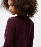 Cardigan de punto color bordó con cuello redondo, cierre frontal de botones de nácar y detalle de volados en la tapeta de botones y el ruedo. Presenta mangas largas con puños ajustados.