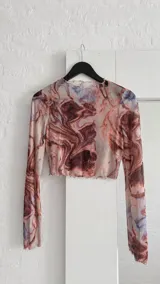 Top de microtul de manga larga con estampado marmolado en tonos marrones y rojizos. Presenta cuello redondo y terminaciones con borde ondulado.