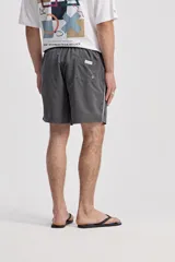 Short de baño oversize gris, con cintura elástica ajustable mediante cordón, bolsillos laterales y detalle de cinta estampada en los laterales.
