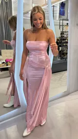 Vestido largo strapless de tejido metalizado en color rosado, con diseño ajustado, tajo lateral pronunciado y detalle fruncido con argolla dorada en la cadera.