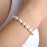 Pulsera de perlas irregulares blancas con pequeñas cuentas doradas intercaladas.