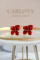 Aros con diseño de flor abierta de cuatro pétalos en color rojo con bordes dorados, fabricados en acero quirúrgico con baño de oro.