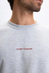 Buzo de cuello redondo color gris melange, con estampa frontal en color bordó con la frase 'STREET TRIPPIN' y logo 'STRP Capsule'. Presenta un diseño de corte holgado con puños y ruedo acanalados.