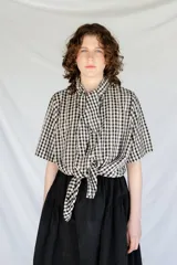 Camisa de algodón a cuadros gingham en blanco y negro, con estampado de broderie blanco, lazo en el cuello, manga corta y corte oversize.