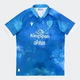 Camiseta de rugby Macron de Uruguay (Teros), modelo 2024, color azul con diseño sublimado que incluye soles de mayo y efecto cielo/nubes. Presenta cuello tipo polo con abertura en V y ribetes blancos en las mangas. Incluye logos de Macron, sponsor Kingspan y Antel, y escudo de la Unión de Rugby del Uruguay (URU).