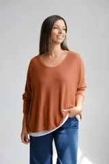 Sweter de punto color terracota con diseño amplio y escote en V con detalle de vivo plateado. Presenta mangas largas y un diseño de doble capa con una base blanca visible en el ruedo.