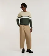Suéter de punto con cuello redondo y manga larga, diseñado con un patrón de bloques de color en tonos beige, blanco y gris. Presenta un corte regular que se ajusta de forma anatómica al cuerpo.