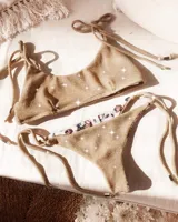 Conjunto de bikini dorado brillante, con corpiño triangular con tiras finas que se atan en los hombros y bombacha colaless reversible que se ata a los costados.