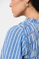 Vestido largo a rayas verticales azules y blancas, con manga globo y diseño de nido de abeja con hilo elástico hasta la cintura. Cuello alto fruncido y falda amplia con caída fluida.