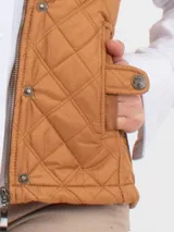 Chaleco beige capitoneado con cierre frontal y cuello de pana marrón.